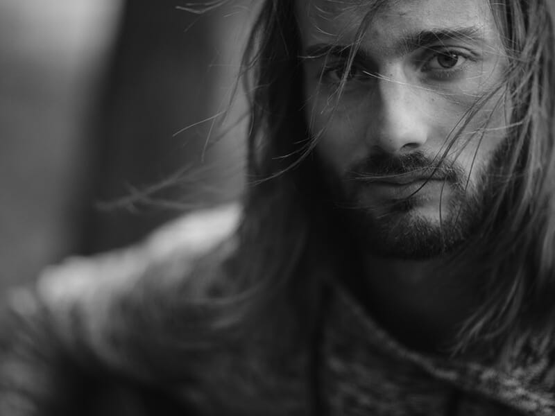 Portrait en noir et blanc d’un homme aux cheveux longs, regard intense et mèches balayées par le vent.