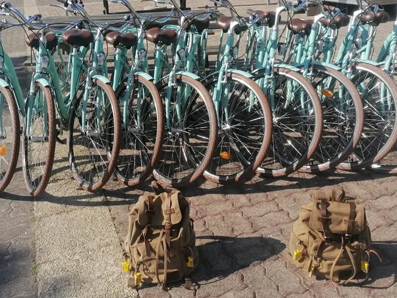 Plusieurs vélos verts alignés avec deux sacs à dos marron posés devant.
