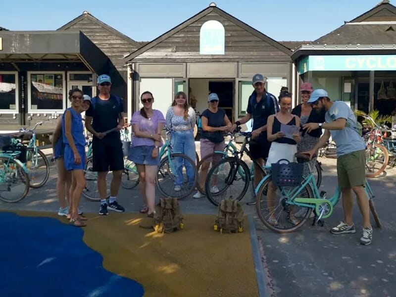 Groupe de personnes avec des vélos devant une boutique, deux sacs à dos au sol.