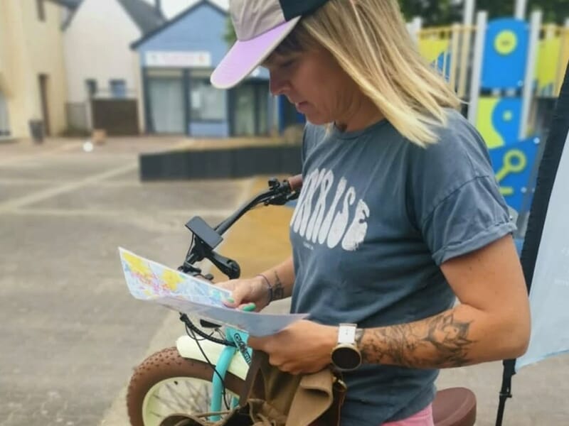 Femme consultant une carte à côté d’un vélo turquoise.