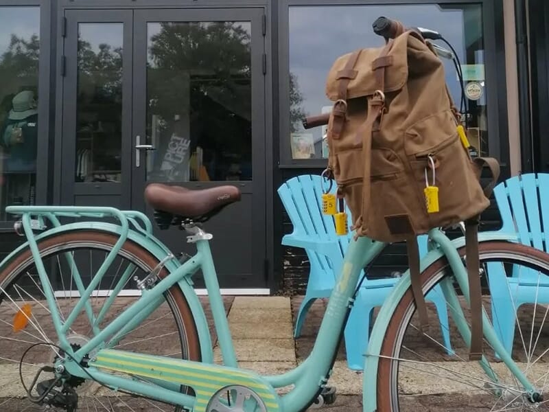 Vélo turquoise garé devant un bâtiment avec un sac à dos marron attaché au guidon.