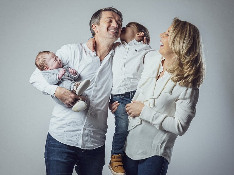 Une famille joyeuse avec deux jeunes enfants et un bébé, tous habillés en blanc, riant ensemble.
