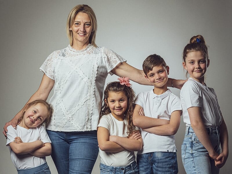 Une femme entoure de ses bras quatre enfants souriants, tous vêtus de blanc et de jeans, dans un esprit familial chaleureux.
