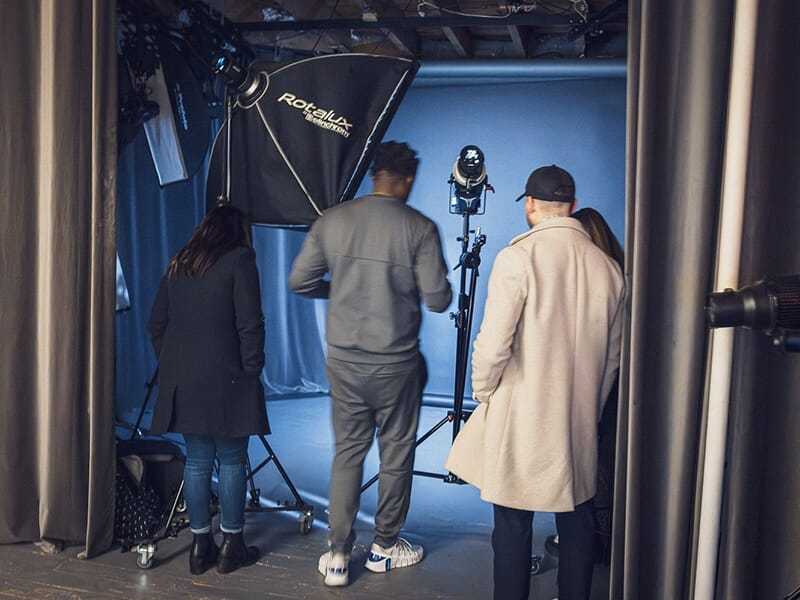 Quatre personnes, vues de dos, observent l’installation d’un éclairage de studio autour d’un fond uni, en pleine séance de formation photo.
