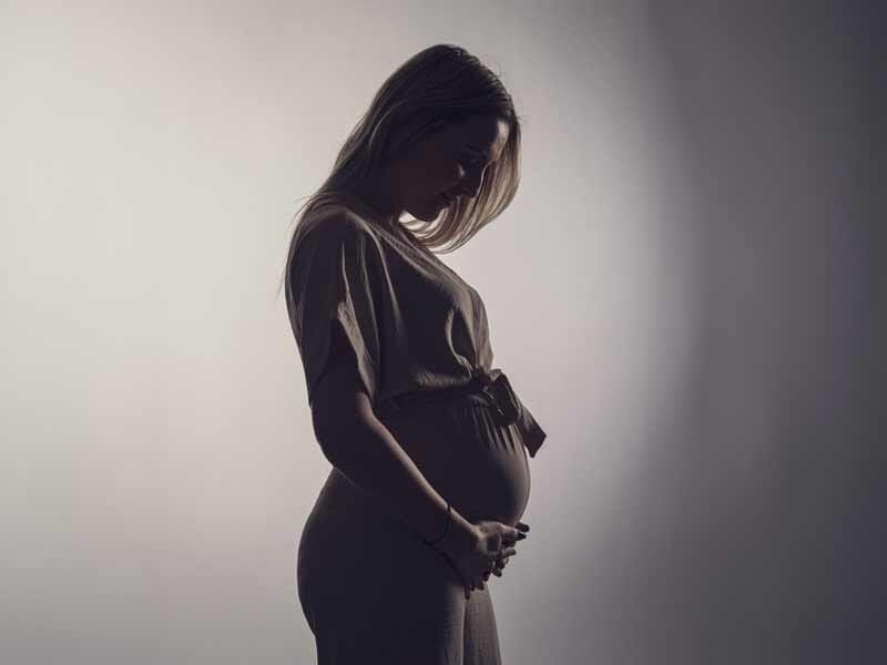 Femme enceinte en robe claire, silhouette en contre-jour, tenant doucement son ventre arrondi.