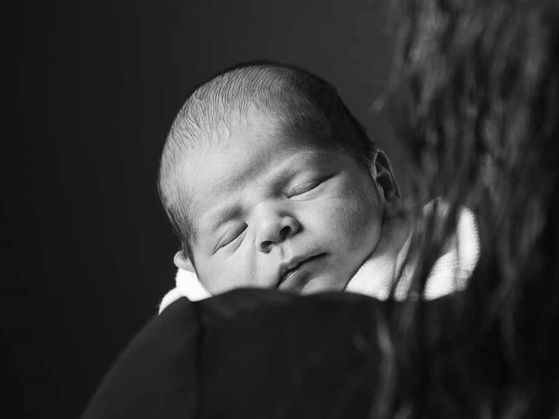 Portrait en noir et blanc d'un bébé endormi, posé sur l'épaule d'un adulte, ambiance douce et intime.