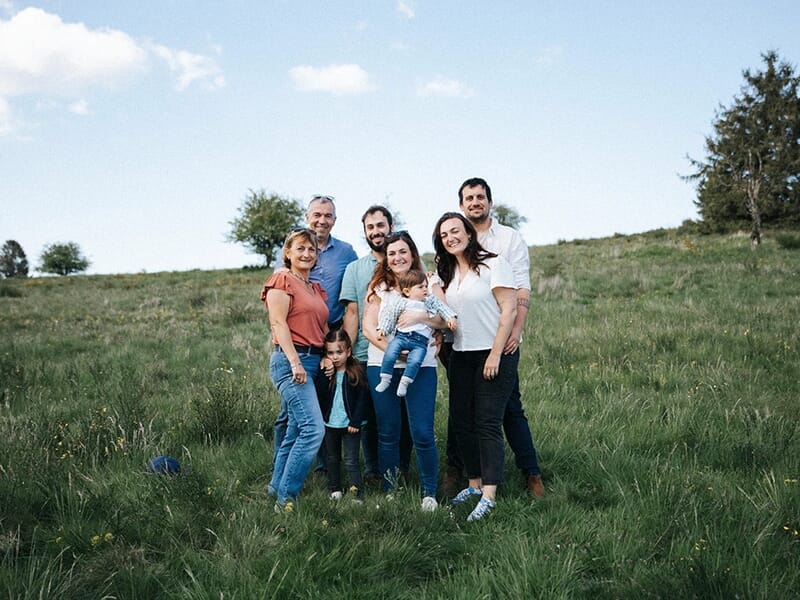 Famille élargie posant ensemble dans un pré verdoyant sous un ciel bleu, plusieurs générations représentées.