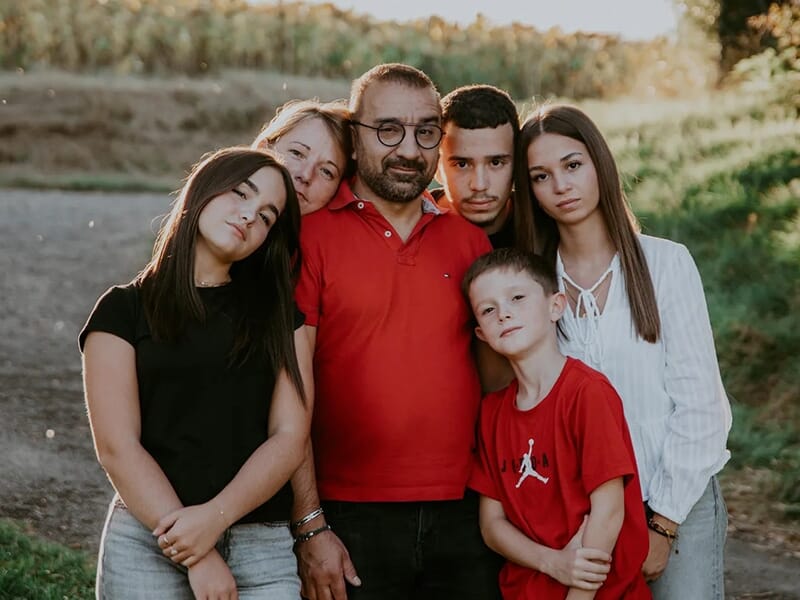 Famille réunie en extérieur en fin de journée, posant de manière proche avec des expressions calmes et tendres.