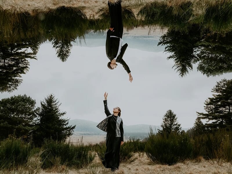 Jeune couple s’embrassant tendrement en extérieur, avec un paysage montagneux et lumineux à l’arrière-plan.