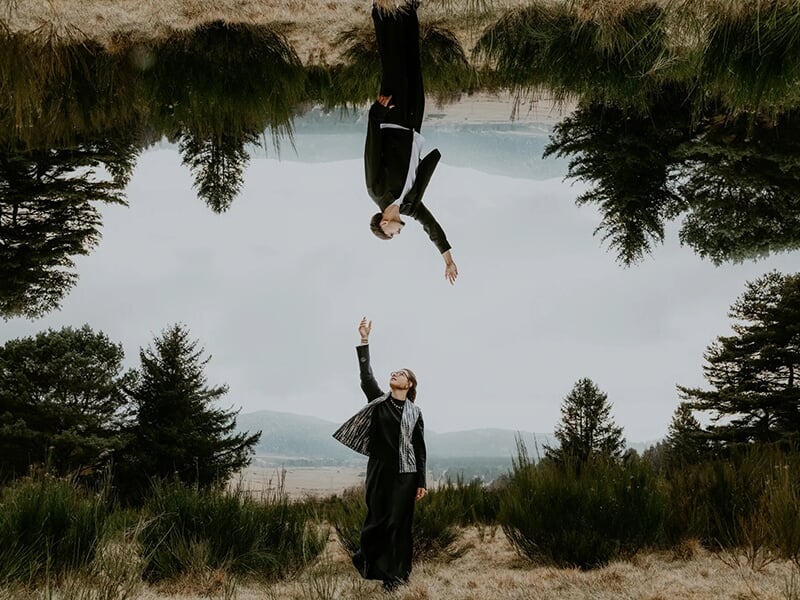  Jeune couple s’embrassant tendrement en extérieur, avec un paysage montagneux et lumineux à l’arrière-plan.