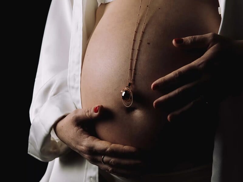 Gros plan artistique sur un ventre de femme enceinte en lingerie blanche, éclairé dans une ambiance sombre.