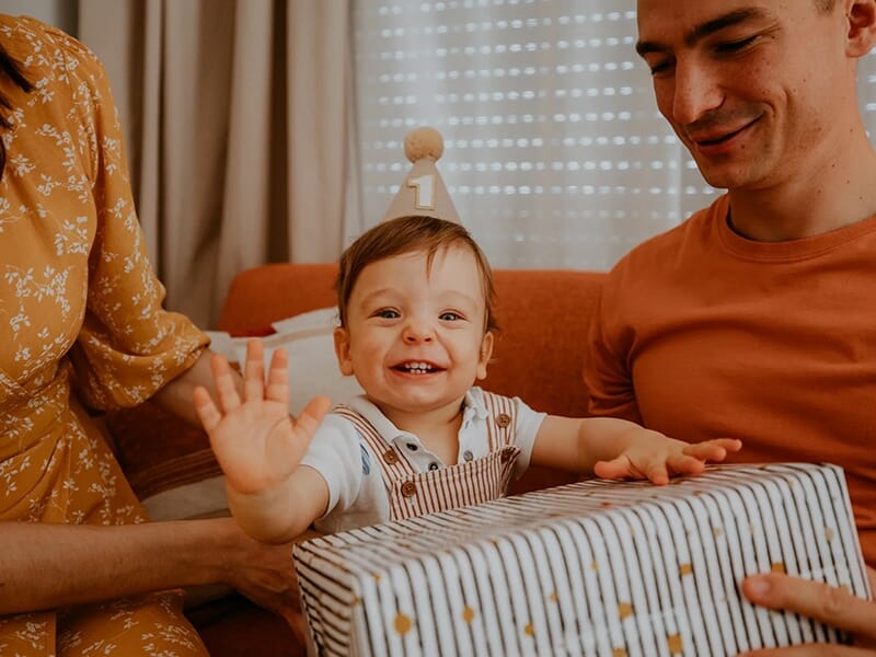 Bébé joyeux fêtant son premier anniversaire, assis avec ses parents et un cadeau devant lui.