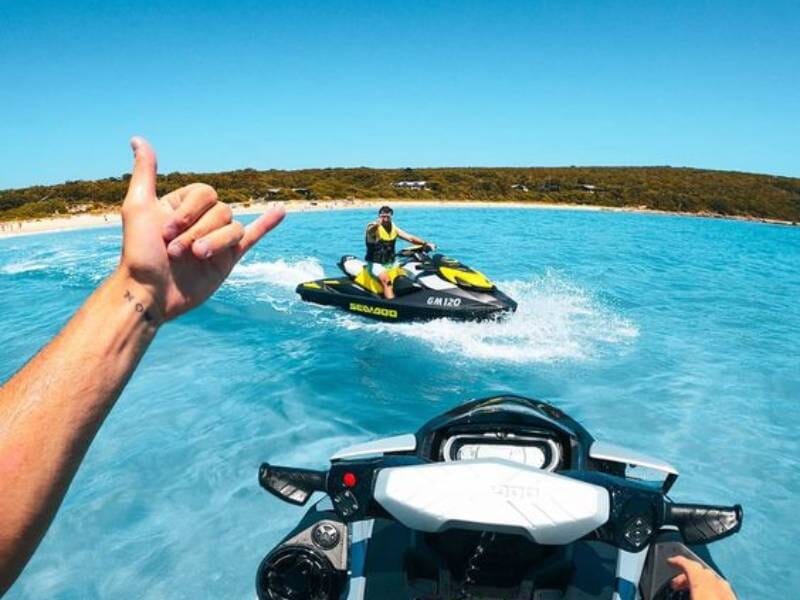 Un homme sur un Jet Ski fait signe à un autre, l'eau est turquoise.