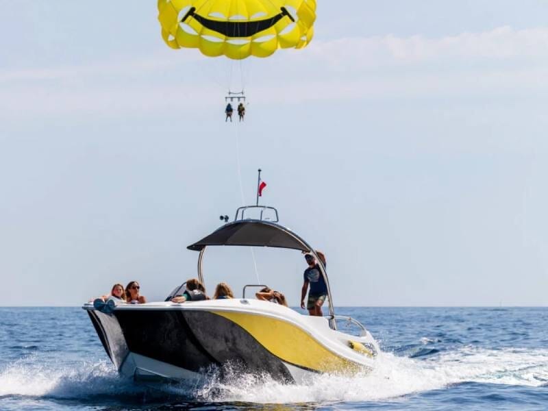 Un bateau traîne un parachute ascensionnel jaune avec deux personnes accrochées en dessous.