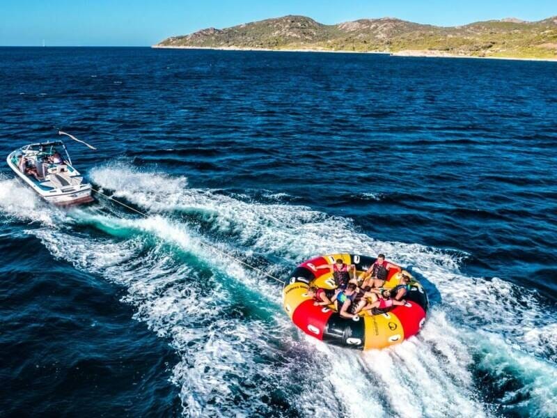 Vue aérienne d'un bateau qui tracte une bouée multicolore avec plusieurs personnes dessus.