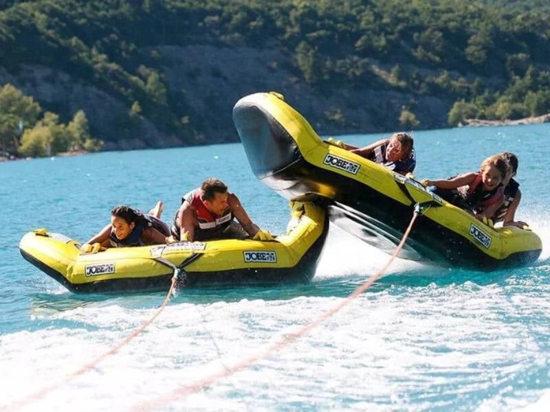Deux bouées tractées jaunes et noires portant 4 personnes se chevauchent sur une eau turquoise.