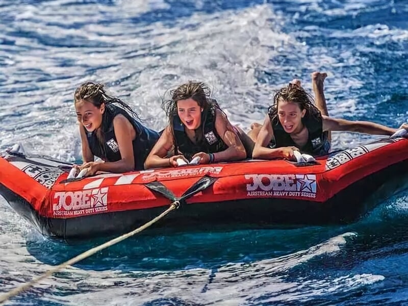 Trois jeunes femmes qui rient sur une bouée tractée rouge et noire.