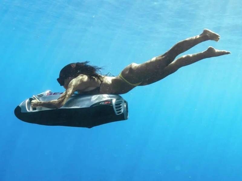 Une femme est sous l'eau, tractrée par un propulseur sous-marin.