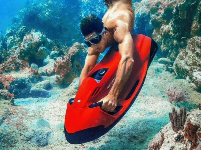 Un homme accroché à un propulseur sous-marin rouge explore les récifs et fonds marins.