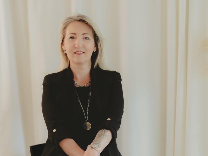 Femme blonde assise, portant un blazer noir et un collier lors d'un shooting avec un photographe de portrait à Lille.