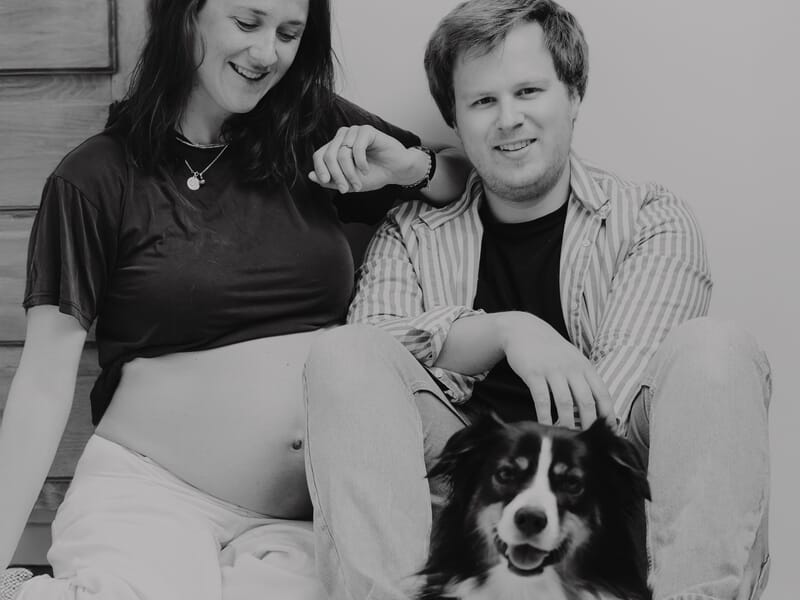 Couple souriant assis au sol avec un chien entre eux lors d'un shooting photo grossesse à Lille.