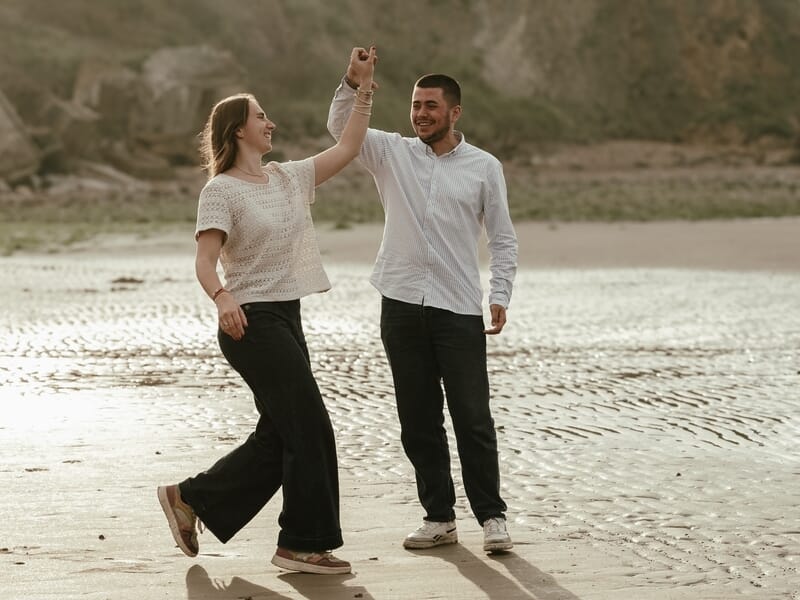 Un couple danse joyeusement sur le sable mouillé lors d'un shooting photo couple sur la Côte d'Opale.