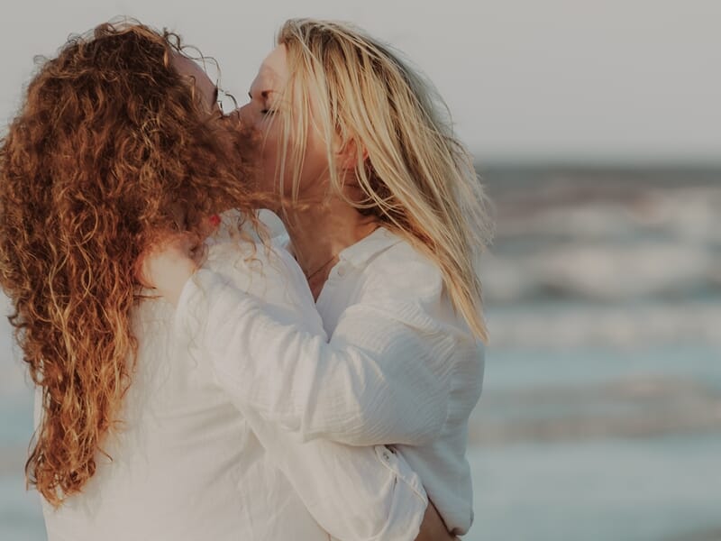 Deux femmes s'embrassent tendrement sur une plage lors d'un shooting photo couple sur la Côte d'Opale.