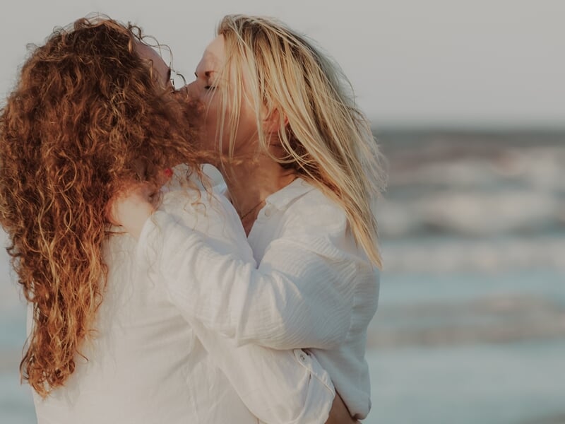 Deux femmes s'embrassent tendrement sur une plage lors d'un shooting photo couple sur la Côte d'Opale.
