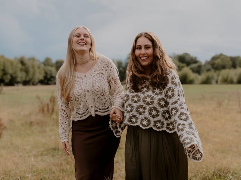 Deux femmes souriantes main dans la main dans un champ lors d'un shooting photo famille.