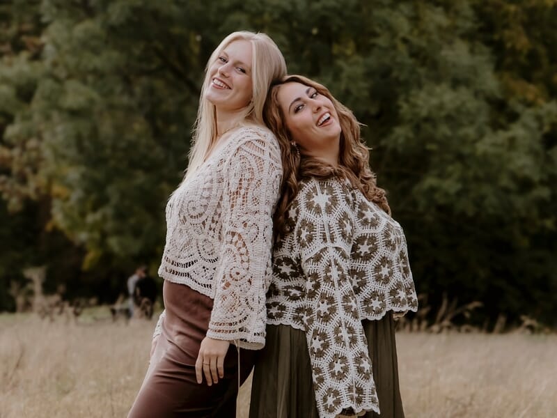 Deux femmes appuyées dos à dos dans un champ lors d'un shooting photo famille.