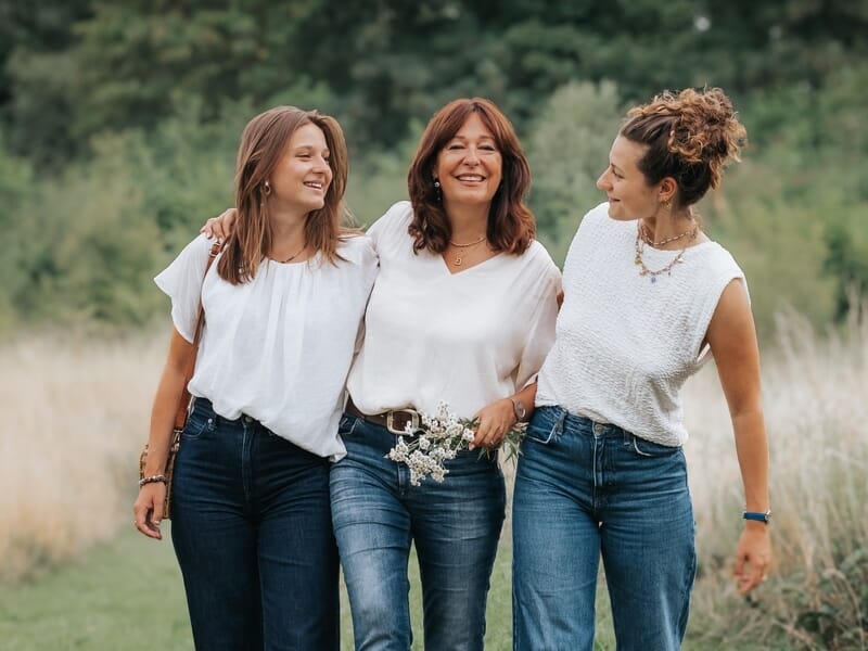 Trois femmes souriantes marchant dans un champ lors d'un shooting photo famille.