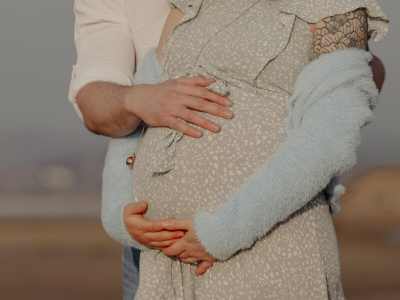 Couple sur la plage, homme et femme enceinte enlacés, mains sur le ventre arrondi, lors d'un shooting avec une photographe grossesse sur la Côte d'Opale.