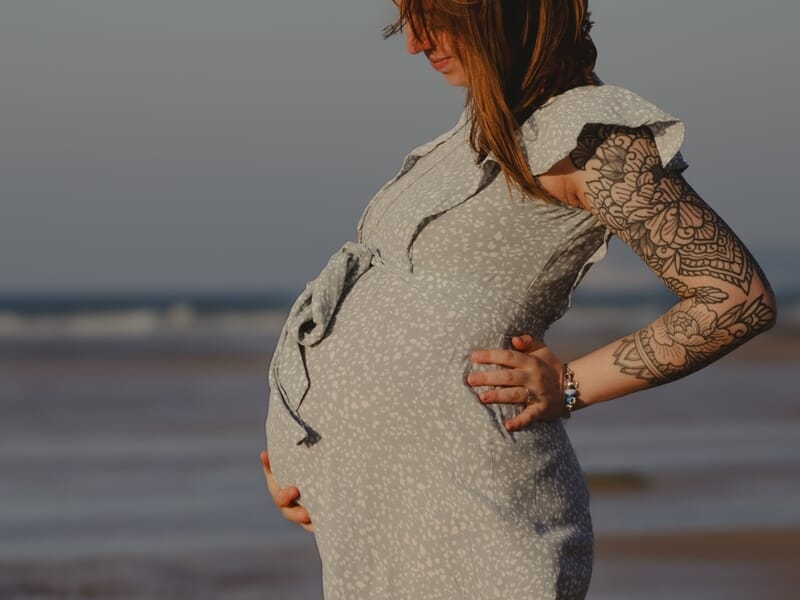 Femme enceinte debout sur la plage, robe légère à motifs, lors d'un shooting avec une photographe grossesse sur la Côte d'Opale.