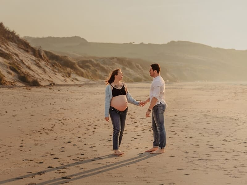 Un couple marche main dans la main sur une plage lors d'un shooting avec une photographe grossesse sur la Côte d'Opale.