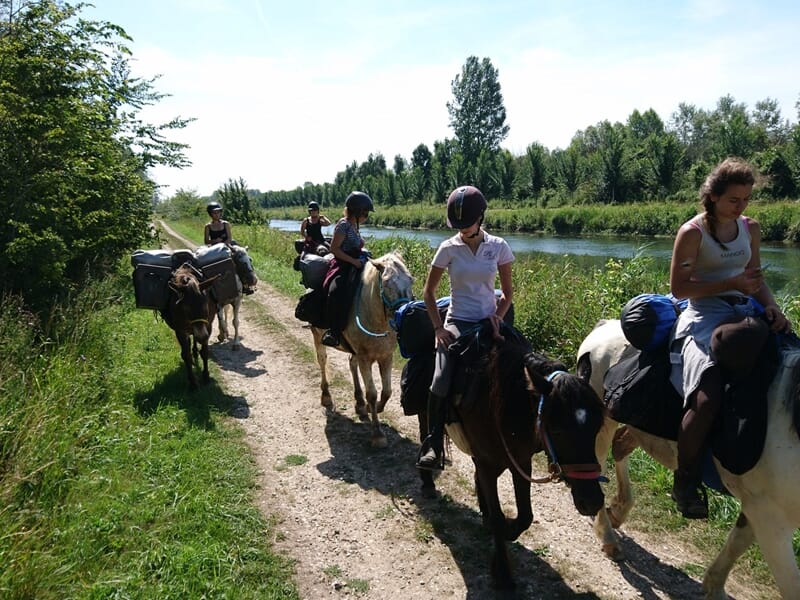 Cavaliers suivant un sentier en bord de rivière, entourés de végétation lors d’une randonnée à cheval