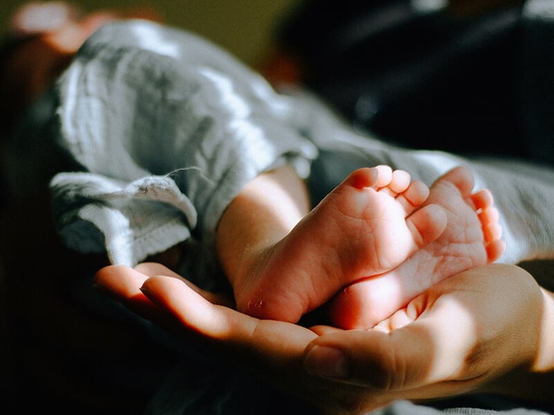Pieds d’un nouveau-né reposant dans la paume d’une main adulte, éclairés par une lumière douce.