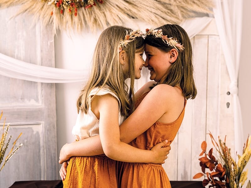 Deux jeunes filles face à face, se tenant dans les bras avec complicité, couronnées de fleurs.