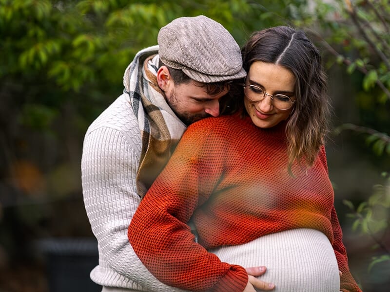 Homme embrassant tendrement l'épaule d'une femme enceinte, les mains posées sur son ventre arrondi.