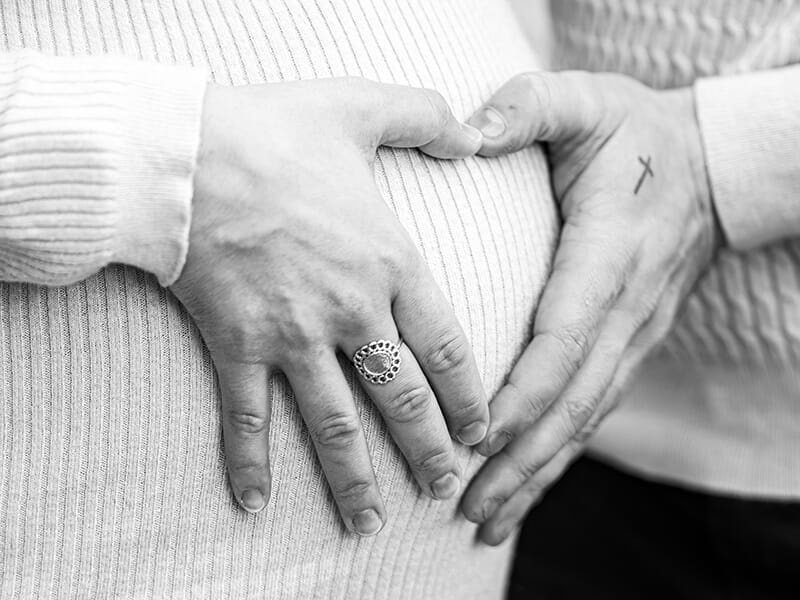Vue rapprochée en noir et blanc de mains posées en forme de cœur sur un ventre de femme enceinte.