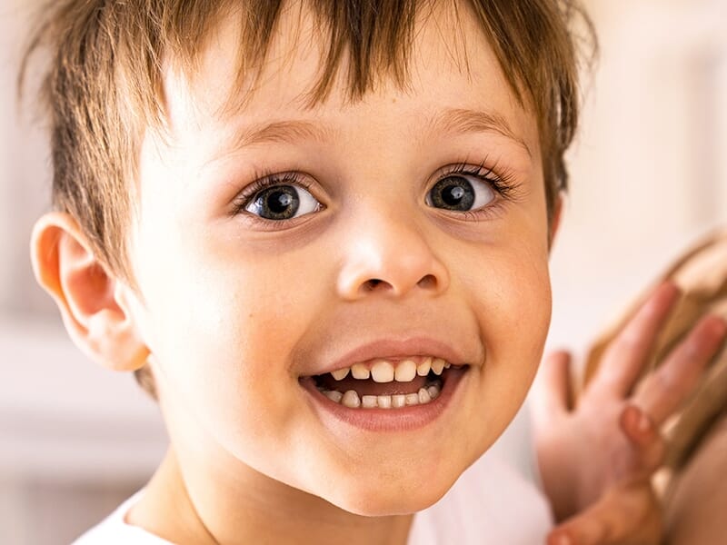 Jeune garçon souriant avec enthousiasme, aux yeux grands ouverts et aux dents visibles.