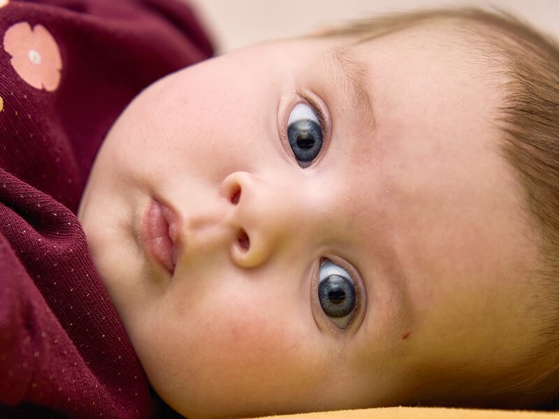 Bébé souriant allongé sur le ventre, portant un haut rayé, entouré de jouets colorés.