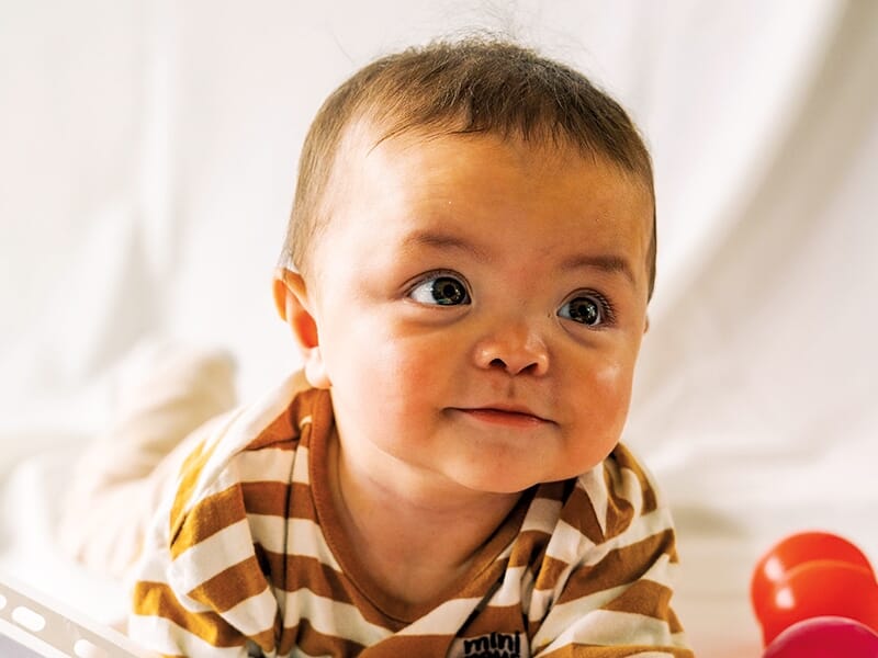 Bébé aux grands yeux allongé sur le côté, regardant intensément l’objectif.