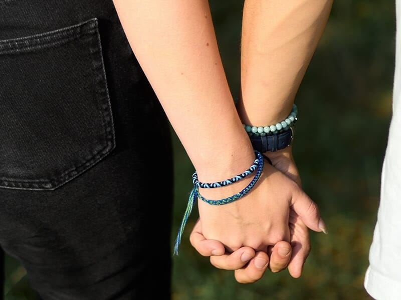 Deux personnes se tenant la main, portant des bracelets bleus assortis, vue rapprochée de leurs poignets.