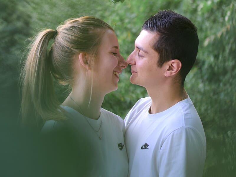 Jeune couple souriant en se regardant tendrement, entouré de verdure.