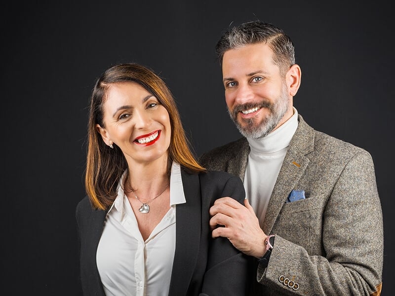 Couple élégant posant en studio, tous deux souriants et bien habillés.