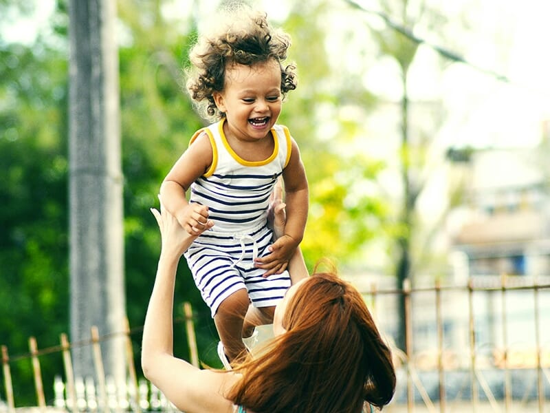 Maman lançant son enfant en l’air dans un moment de jeu joyeux en extérieur.