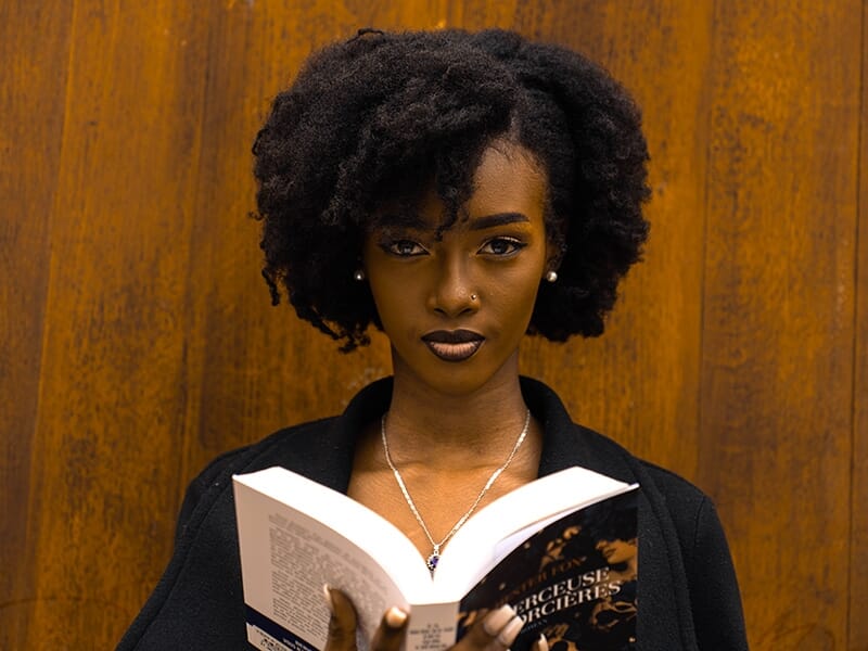 Femme tenant un livre ouvert et regardant l’objectif avec intensité.