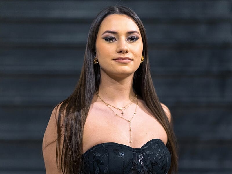 Femme en robe noire élégante posant avec assurance devant un fond sombre.