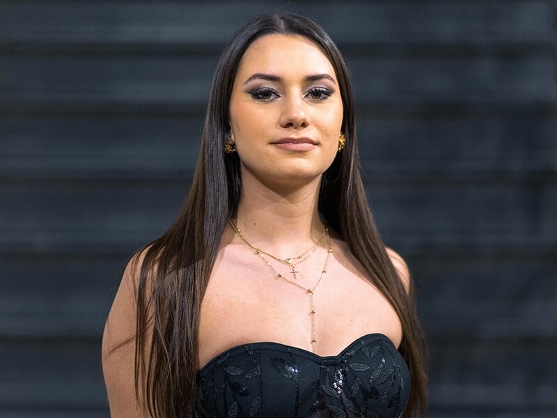 Femme en robe noire élégante posant avec assurance devant un fond sombre.