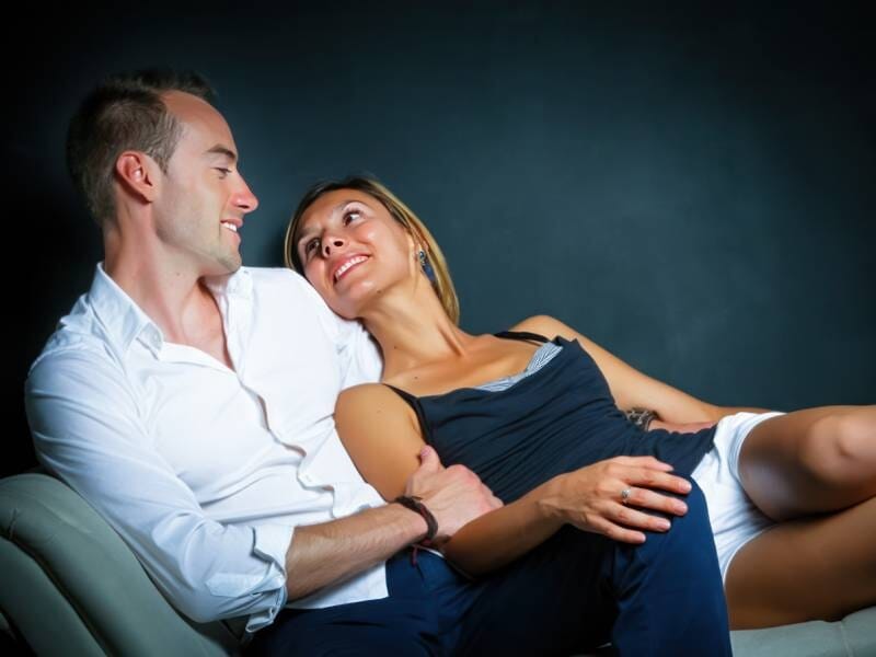 Un couple est installé dans un canapé et se regarde amoureusement dans les yeux.